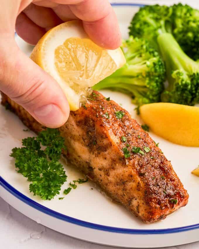 squeezing a lemon wedge over a cajun salmon filet on a plate.