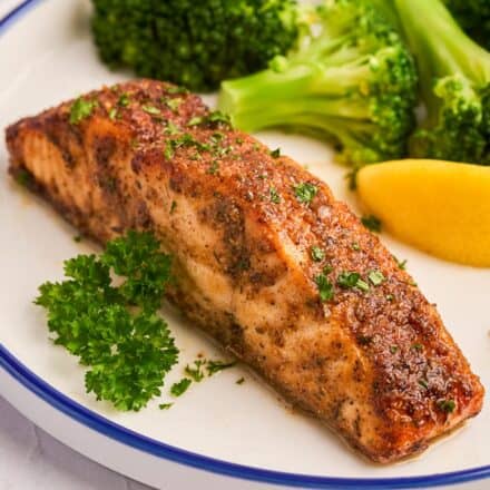 cajun salmon filet on a plate with broccoli florets and a lemon wedge.