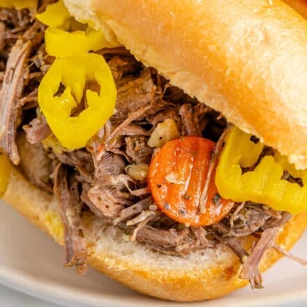 close up photo of Italian beef on a hoagie bun, topped with peppers.