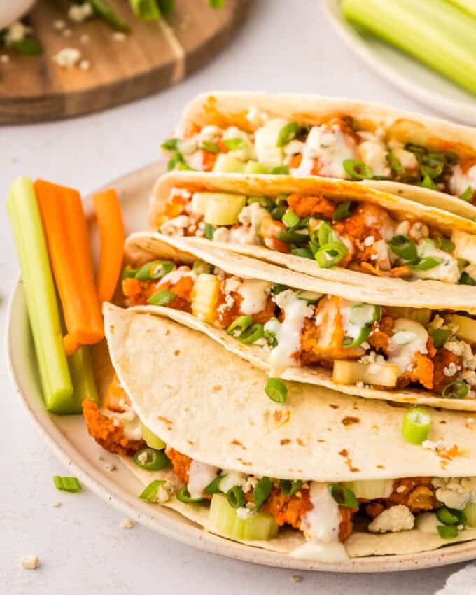 pile of buffalo chicken tacos on a white plate with carrots and celery.