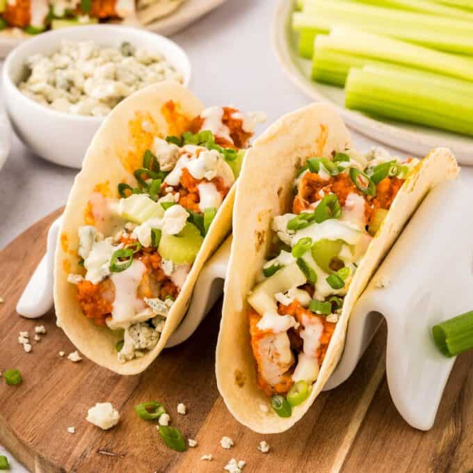 two buffalo chicken tacos on a wooden cutting board.