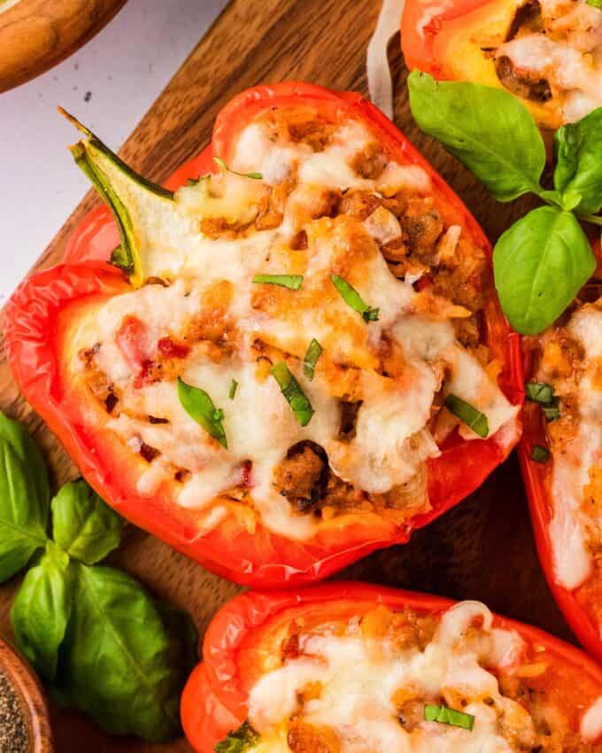 several stuffed peppers on a wooden platter with fresh basil.