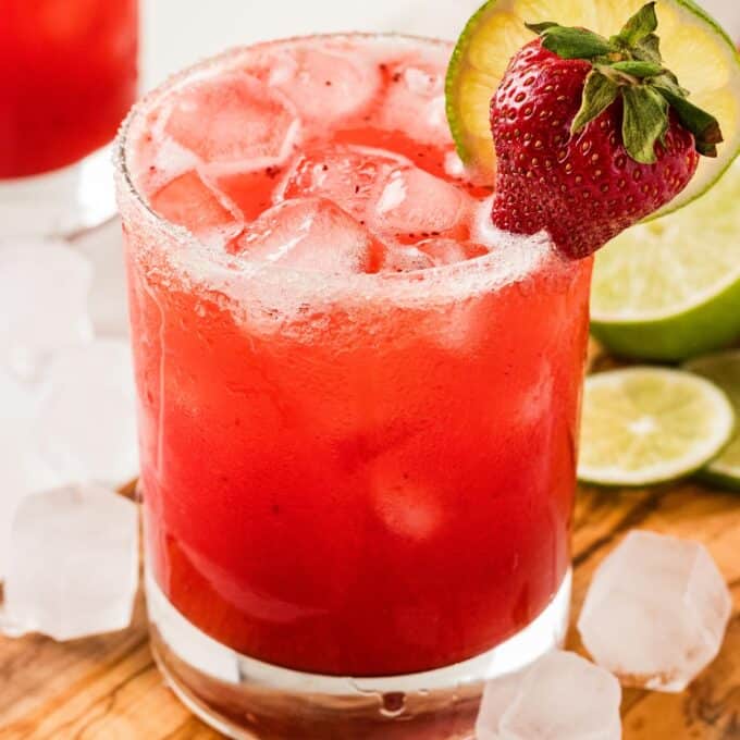 strawberry margarita on a wooden cutting board with limes.