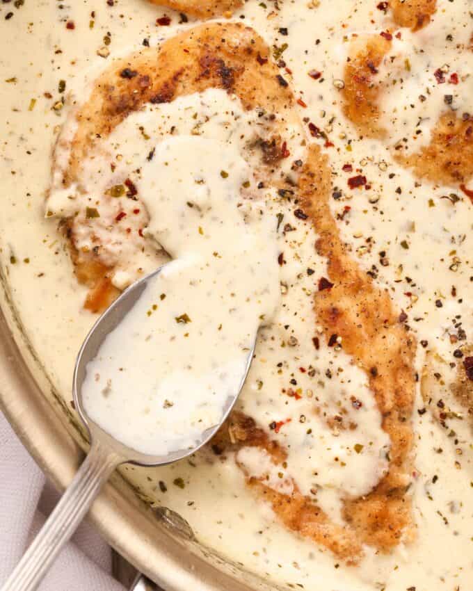 spooning pesto cream sauce over chicken breasts in skillet.