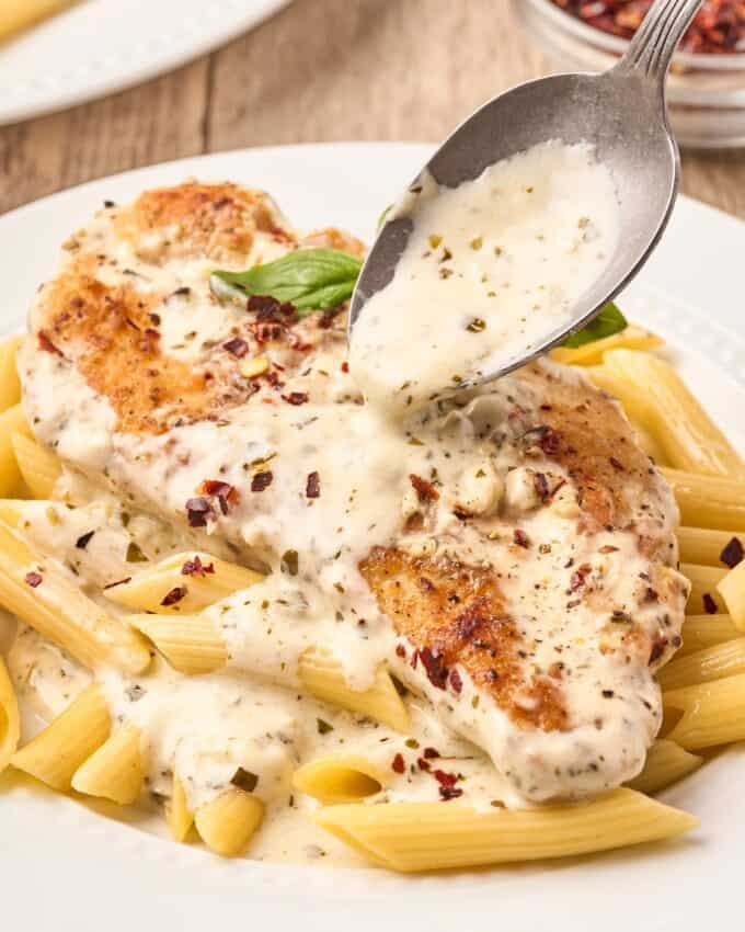 chicken breast on a bed of penne with pesto cream sauce spooned over the top.