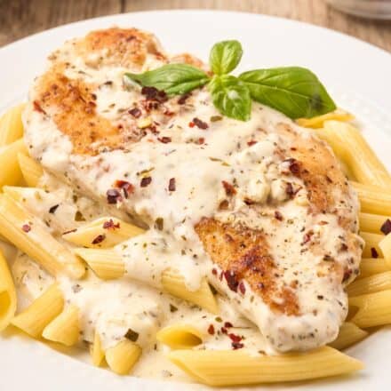 creamy pesto sauce drizzled over chicken breast on a bed of penne pasta