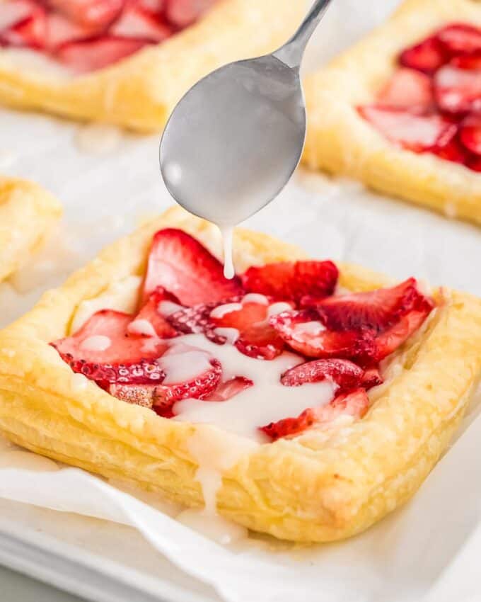 drizzling a strawberry danish with a sweet glaze.