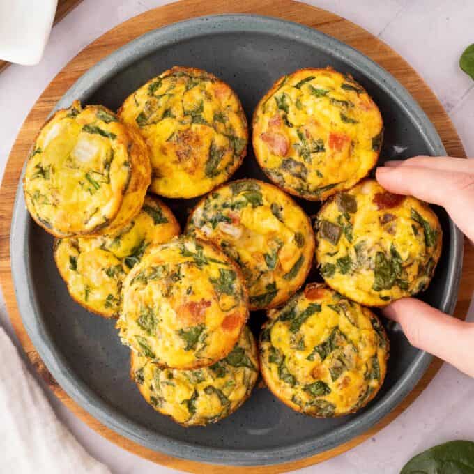 plate full of egg bites with a hand reaching out to grab one.