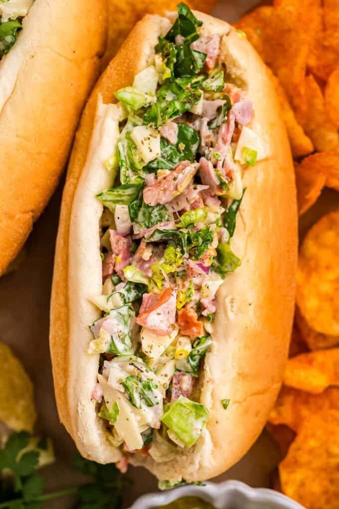 close up photo of a chopped salad sandwich surrounded by chips.