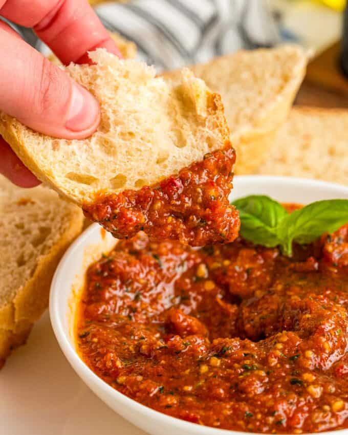 dipping a piece of crusty bread into pesto.