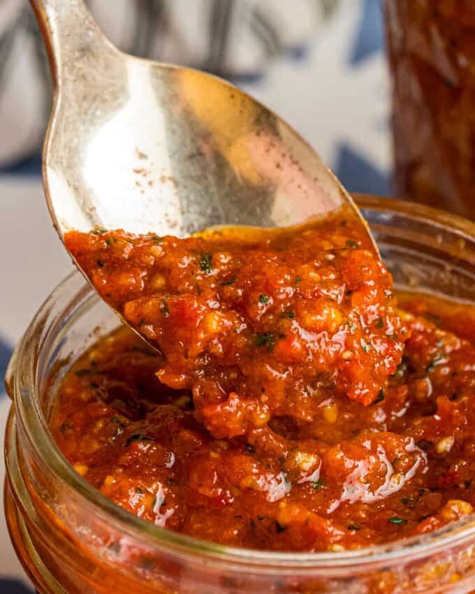 spooning sun-dried tomato pesto into a mason jar.