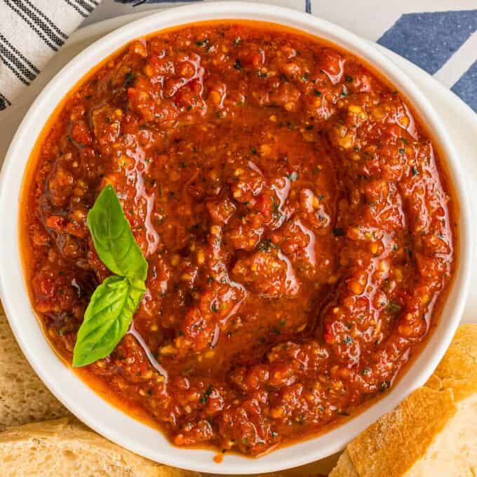 overhead photo of a white bowl filled with sun-dried tomato pesto and garnished with a basil leaf.