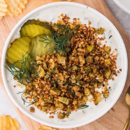 overhead photo of fried pickle dip garnished with pickles and dill, in white bowl.