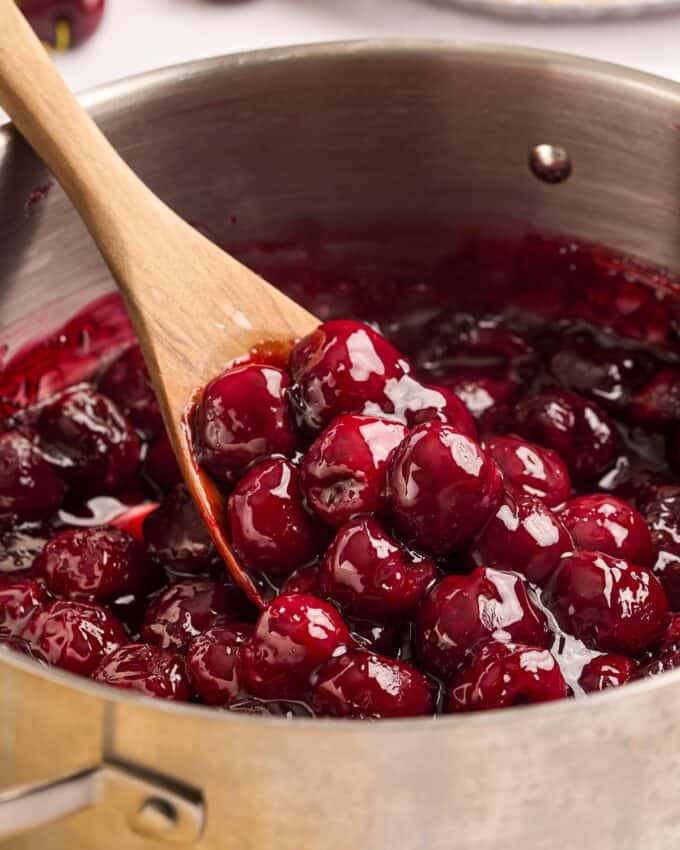 stirring cherry pie filling with a wooden spoon.