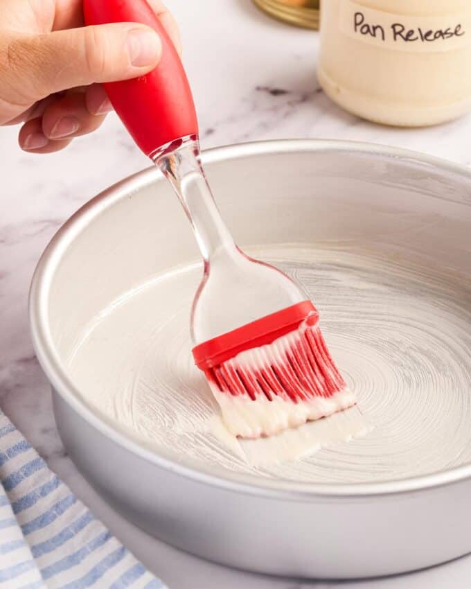 brushing a cake pan with pan release with a pastry brush.