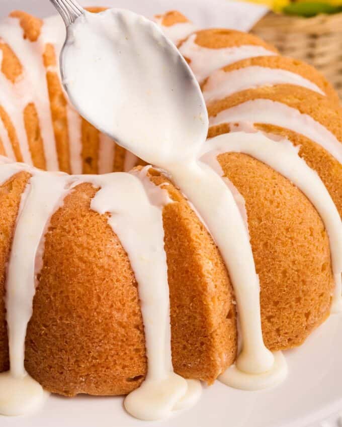 spooning lemon glaze over the top of a lemon bundt cake.