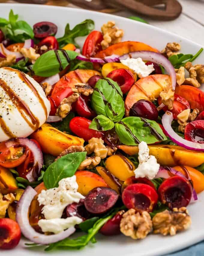 white platter of burrata salad with peaches and cherries