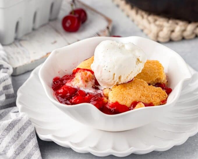 white bowl of cherry cobbler on a white plate