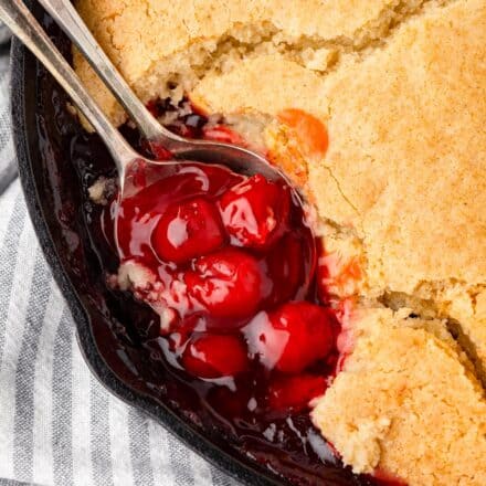 cherry cobbler topped with a cake-like crust in a cast iron skillet.