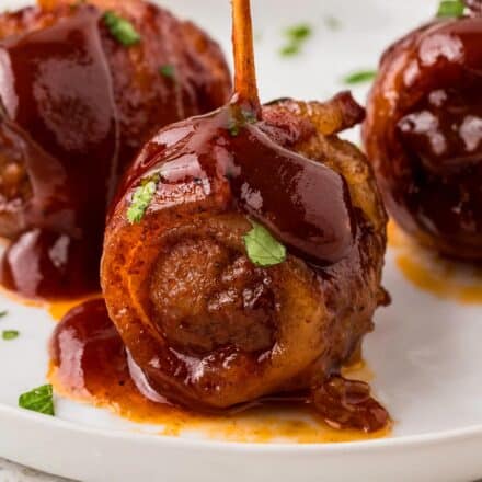 several bacon wrapped bbq meatballs on a white plate, speared with toothpicks.