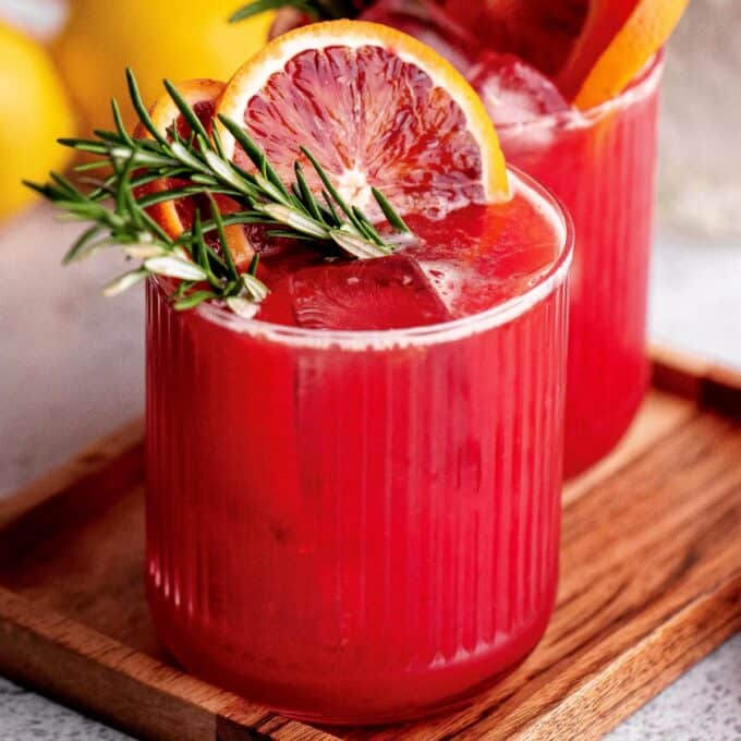 two blood orange whiskey cocktails on a wooden tray.