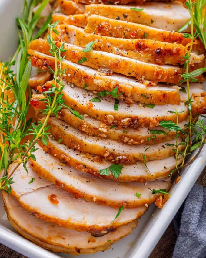 sliced turkey breast on white platter with herbs and oranges.