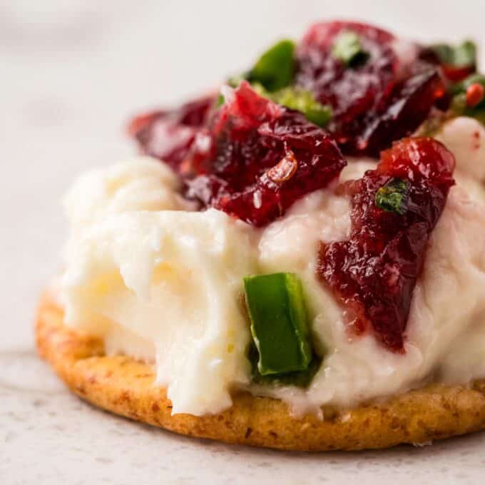 close up photo of a cracker topped with cream cheese dip with cranberries and jalapeños