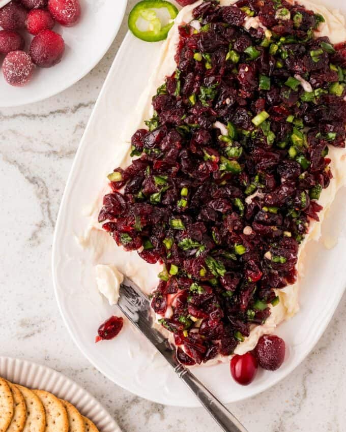 white oval platter with cranberry jalapeño cream chees dip with a cheese knife.