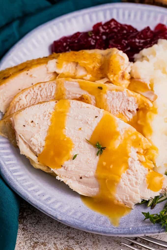 slices of roasted turkey with gravy on white plate with sides.