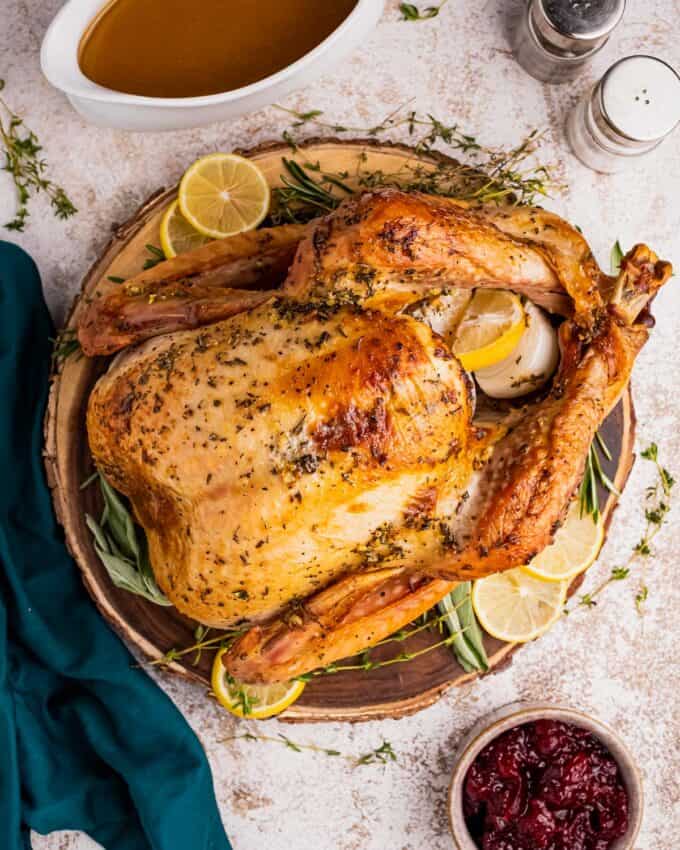 round wooden platter with roast turkey surrounded by herbs and citrus.