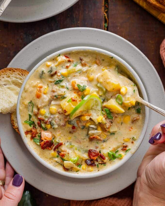 enjoying a bowl of poblano corn chowder with a piece of bread and a spoon.