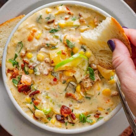 dunking a piece of bread into a white bowl of poblano corn chowder