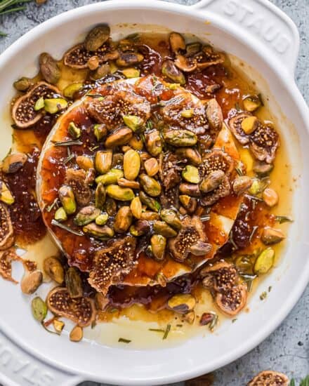 This honey herb and fig baked brie recipe is perfect for the holidays, or any party! A wheel of brie is topped with sweet fig jam, fresh rosemary, dried fig slices, salty pistachios, and sticky honey, then baked until perfectly gooey. Serve with baguette slices, apples, crackers, and more!