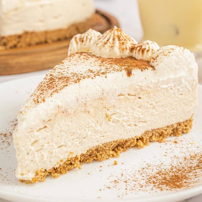 slice of eggnog no-bake cheesecake on a white plate dusted with cinnamon and nutmeg.