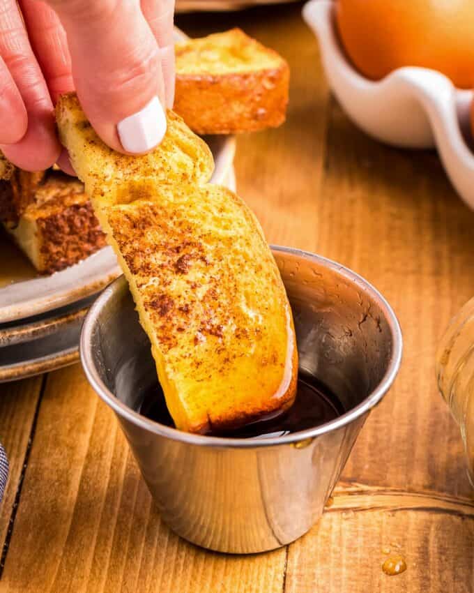 dipping a piece of french toast into a small cup of syrup