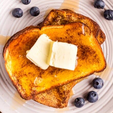 two slices of french toast on a white plate with butter and syrup and blueberries