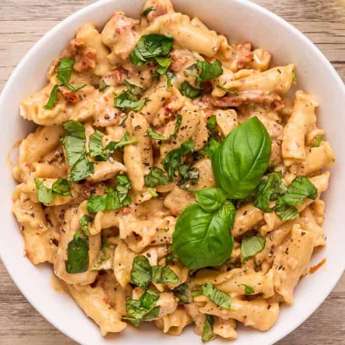 overhead photo of marry me chicken pasta in a white bowl with basil leaves