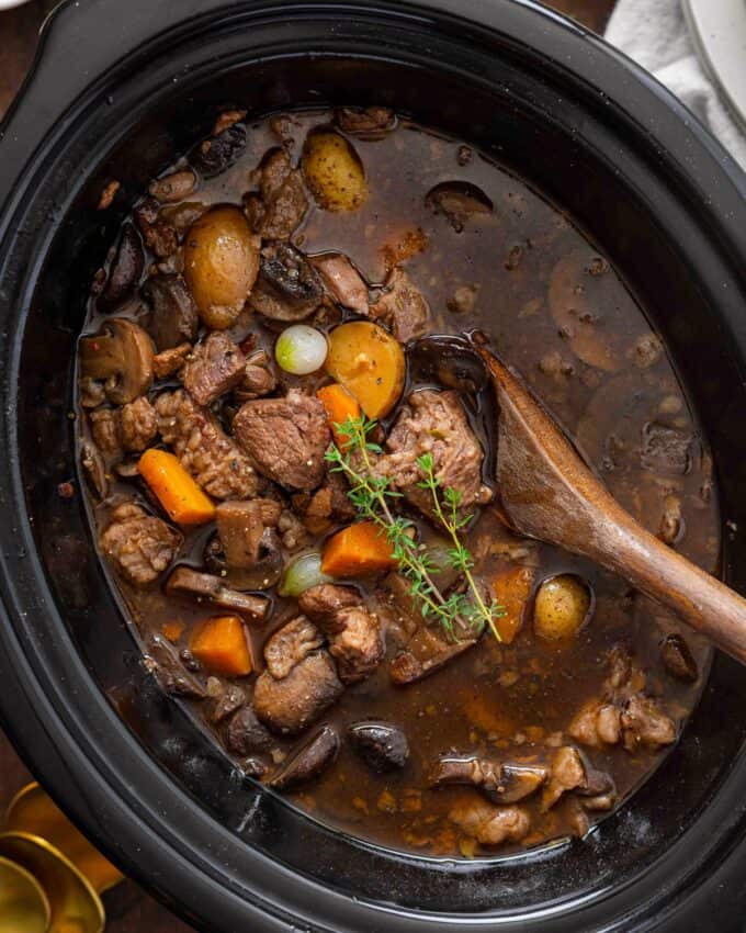 beef bourguignon in a slow cooker with a wooden spoon.